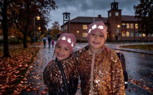 To piger med lyserøde reflekshuer foran skolen på en mørk efterårsdag for optimal trafiksikkerhed.