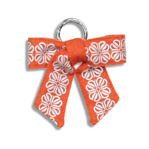 Smart reflex till väskan i form av en rosett. I orange med reflexmönster av fyrklöver.