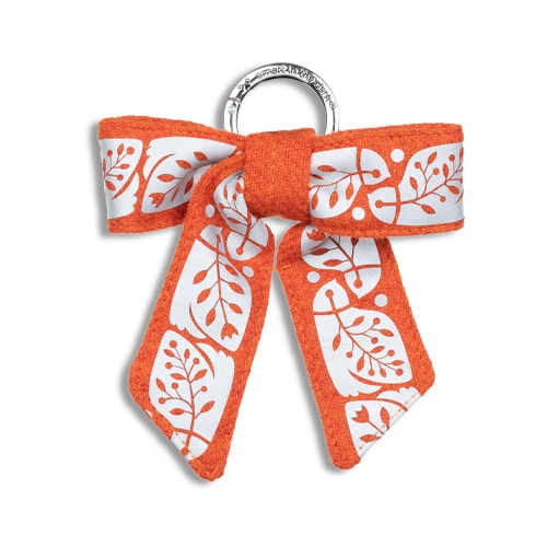 Vackert smycke till väskan i form av en reflexrosett. I orange med reflexmönster av nattskärra.